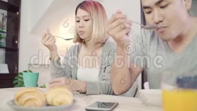 漂亮的亚洲年轻夫妇在吃早餐时，一边拿着报纸和手机，一边在桌子上分心。